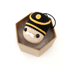 a crocheted stuffed animal wearing a hat in a wooden box on a white background