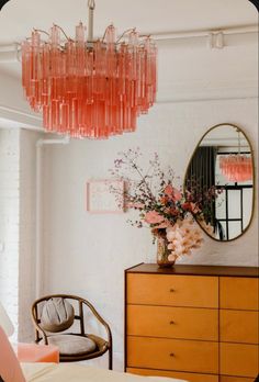 a pink chandelier hangs from the ceiling above a dresser with flowers in it