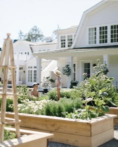 two women in front of a large white house with lots of plants and flowers around them