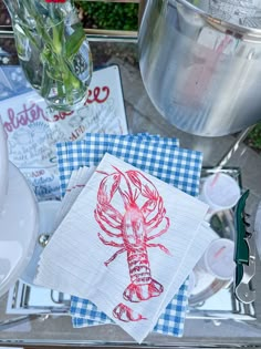 a table topped with plates and napkins covered in red lobster artwork next to a potted plant