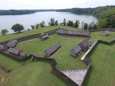 an aerial view of a large grassy area with several buildings and water in the background