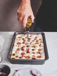 a person is pouring olives into a square casserole dish with onions on the side