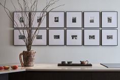 a vase with some branches in it sitting on a counter next to pictures and cups