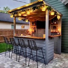 an outdoor bar with stools and lights on the outside wall, in front of a house