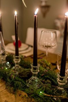 candles are lit on a table with greenery