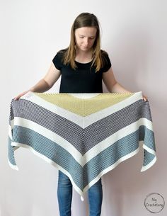 a woman is holding up a blanket that has been made from strips of yarn on it