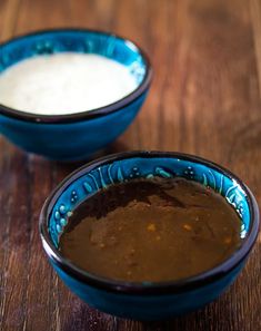 two blue bowls filled with food sitting on top of a wooden table next to each other