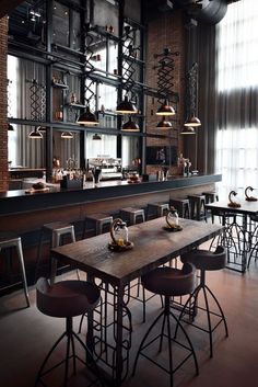 an empty restaurant with tables and stools in front of a bar area that has shelves on the wall