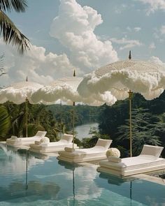 an outdoor pool with lounge chairs and umbrellas on the side by the water, surrounded by palm trees