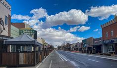 an empty street with shops and businesses on both sides, under a cloudy blue sky