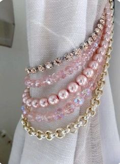 three strands of pink pearls are attached to a white curtain with gold chains on it