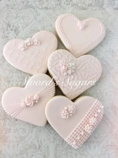 four decorated heart shaped cookies sitting on top of a white tablecloth with lace and flowers