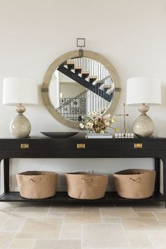 a black console table with baskets under it and a mirror above it on the wall