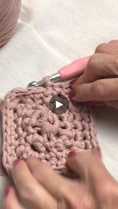 a woman is crocheting a square with pink yarn