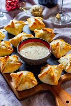 small pastries with dipping sauce in a bowl on a cutting board next to wine glasses