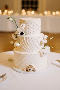 a three tiered white wedding cake with flowers on the top and bottom, sitting on a table