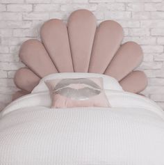 a white bed topped with a pink pillow sitting next to a brick wall and headboard