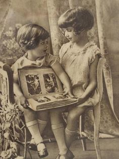 an old photo of two young children sitting on a chair with pictures in their lap