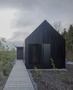 a wooden walkway leading to a black building with text that reads format eff investies dark barn - shaped houses into bavarian forest