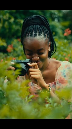 a woman holding a camera up to her face and looking through the bushes in front of her