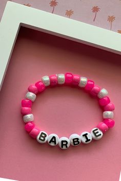 a pink and white bracelet with the word barbie written on it in small letters that spell barbie