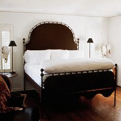 a bed with white sheets and pillows in a bedroom next to two lamps on either side of the bed