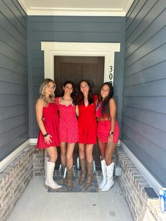 four young women in red dresses standing on the front steps of a house with white boots