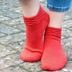 a person wearing red socks and blue jeans standing on cobblestone with their feet in the air