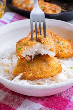 two pieces of fried fish on top of rice in a bowl with a fork stuck into it