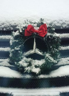 a mercedes wreath on the hood of a car covered in snow with a red bow