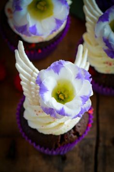 cupcakes with white icing and purple flowers on top are sitting on a wooden table