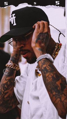 a man with tattoos on his arms and hands is talking on the phone while wearing a hat