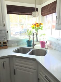 a kitchen with white cabinets and countertops has sunflowers in the window sill