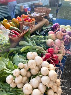 many different types of vegetables are on display at an outdoor farmers market, including turnips and radishes