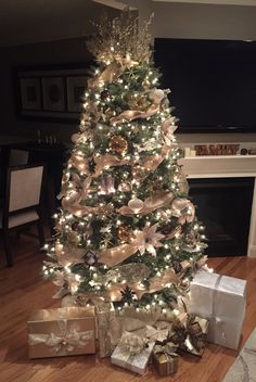 a christmas tree is decorated with gold and silver ribbons, bows, and lights in front of a fireplace