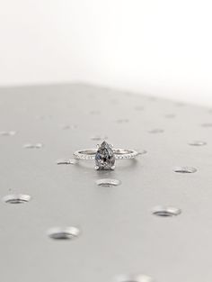 a white diamond ring sitting on top of a metal surface with drops of water around it