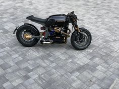 a black motorcycle parked on top of a stone floor next to a parking lot with no people