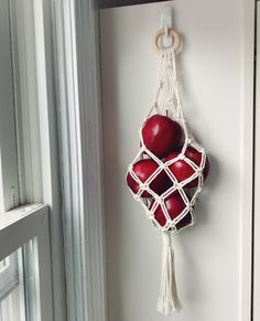 two red apples are hanging from a white string and hang on the wall next to a window