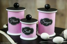 three pink canisters with black labels on them and white balls in the middle