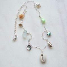 "This beautiful ocean inspired necklace features a sliced cowrie shell in the center with various shells, a white pearl and frosted glass dangling from a sterling silver 1.6mm long and short chain. Available in 18\" or 24\" lengths. Shells include pyrene, nassa, abalone, tapok, puka Also available in gold filled" Shell Necklace Silver, Silver Shell Jewelry With Pearl Charm, Beach Jewelry: Silver With Pearl Charm, Beach Jewelry With Silver Pearl Charm, Silver Beach Jewelry With Pearl Charm, Beach Silver Jewelry With Pearl Charm, Silver Jewelry With Pearl Charm For Beach, Ocean-inspired Silver Shell Necklace, Silver Dangle Jewelry With Shell