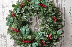 a christmas wreath hanging on the side of a wooden wall with red berries and green leaves