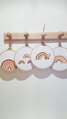 four embroidery hoops hanging from a wooden hanger on a white wall with three different designs