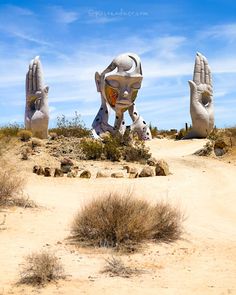 three large hand sculptures in the desert with blue sky