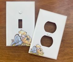 two light switch plates sitting on top of a wooden table with cartoon characters painted on them