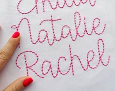 a woman's hand is stitching the letters in red thread