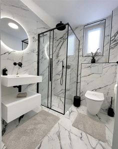 a white bathroom with marble walls and flooring, including a walk in shower next to a toilet