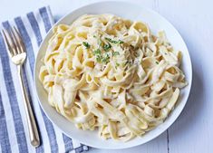 a white plate topped with pasta covered in sauce and parsley next to a fork