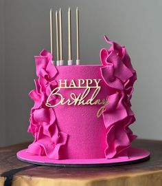 a pink birthday cake with gold lettering and ruffles