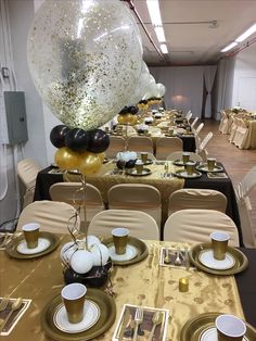 a table set up for a party with black and gold decorations, balloons and plates