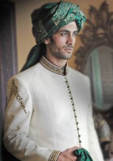 a man in a white suit and green turban standing next to a mirror